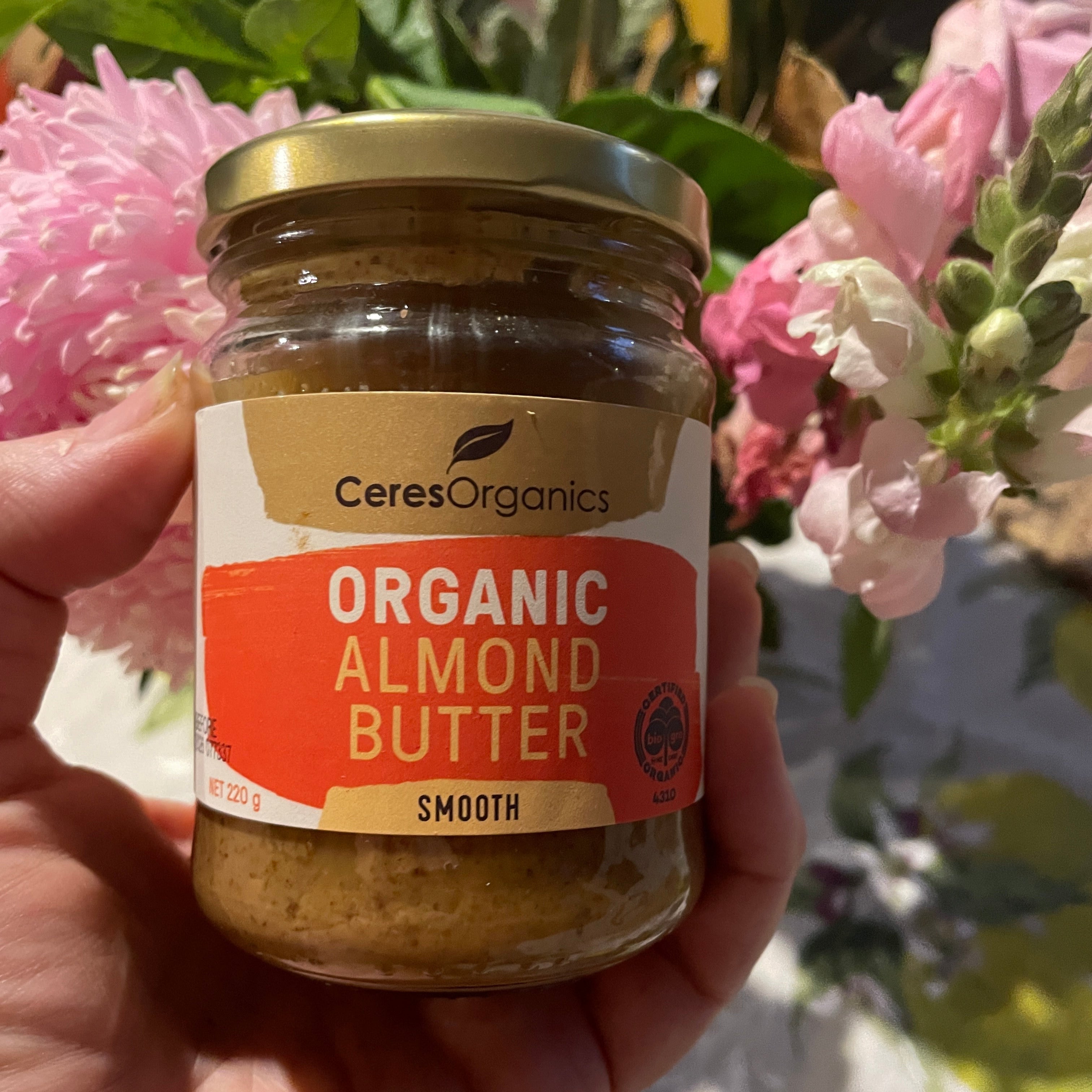 Hand holding a jar of Ceres Organics Organic Almond Butter in front of flowers